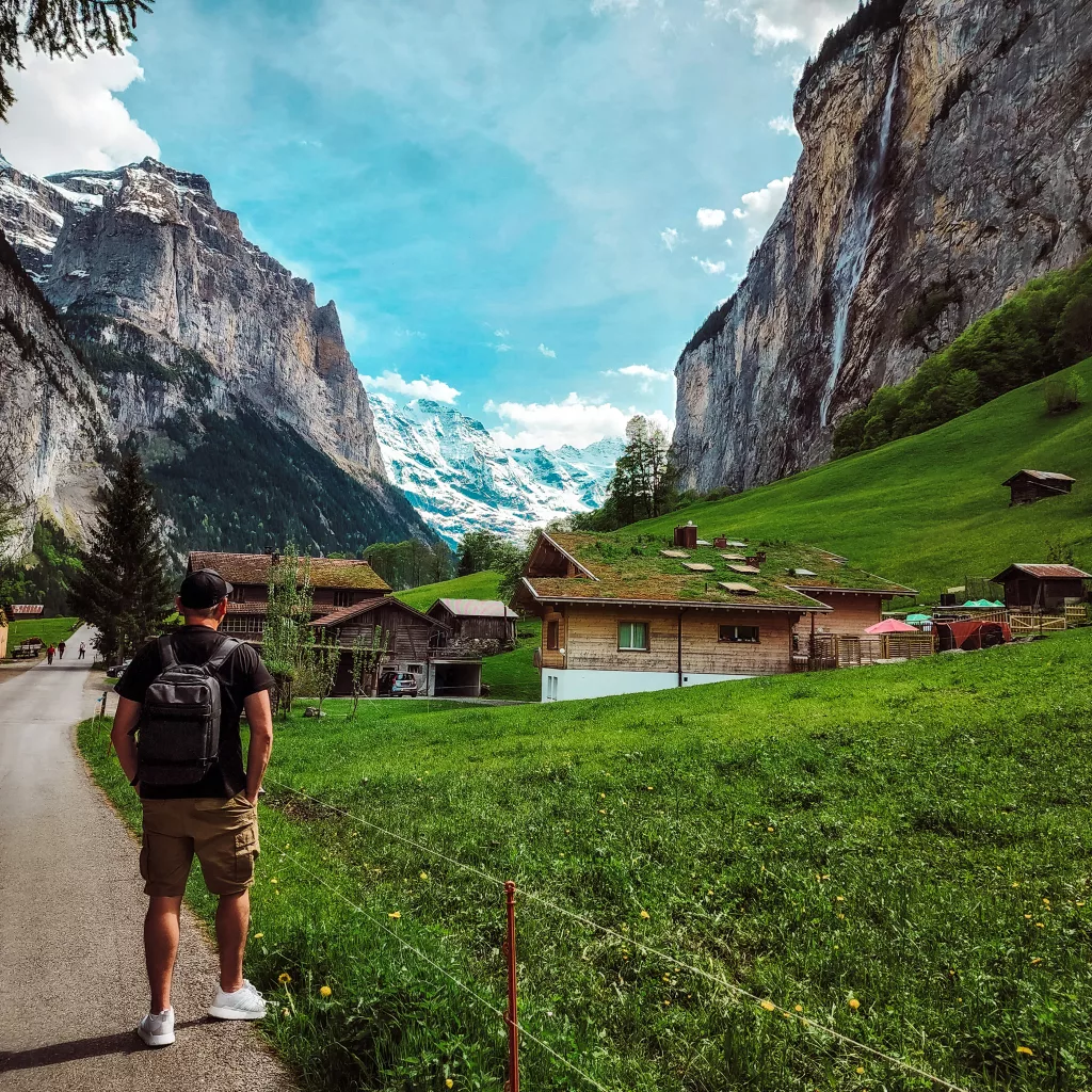  Mike walking out through lush green fields toward waterfalls and snow capped mountains. Why you should visit spectacular Lauterbrunnen Valley